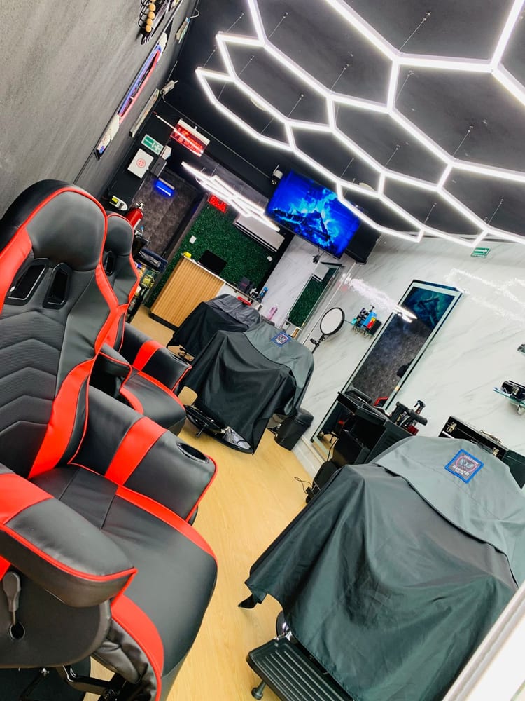 Interior del local: sillones gamer rojo y negro, iluminación LED hexagonal y estaciones de barbería